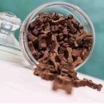 a jar of natural dog treats tipped on its side with dark brown soft dog treats that are shaped like a bone spilling out